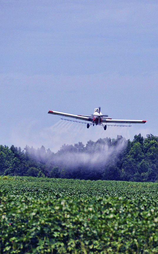 Image of airplane in flight spraying pesticide over farming crop  